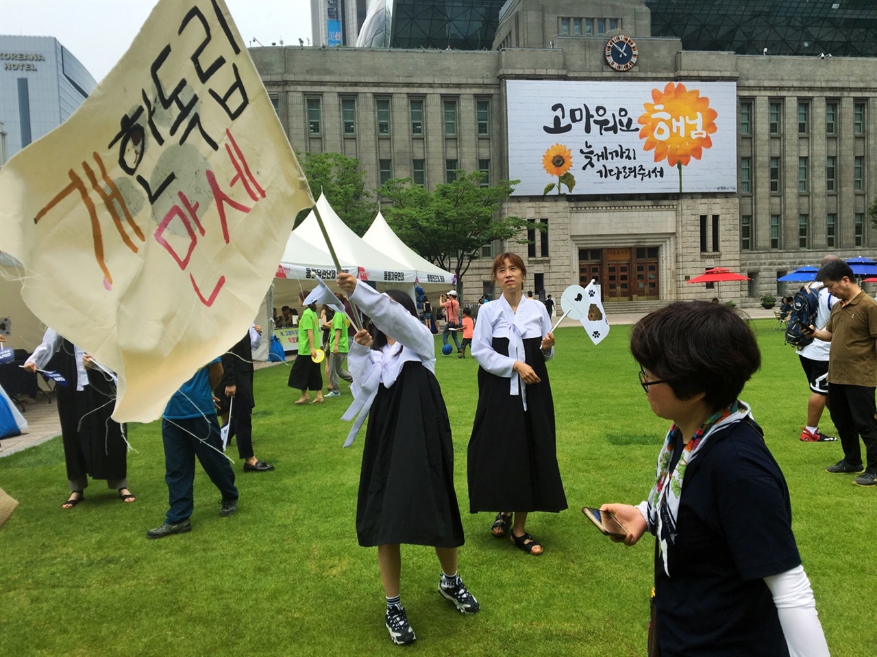  지난 7월 9일 서울 시청 광장에서 있었던 'STOP IT-이제 그만 잡수시개' 행사가 있었다. 이 행사에 참여한 한 행사자는 한복을 입고 큰 깃발을 흔들면서 퍼포먼스를 진행하고 있다.