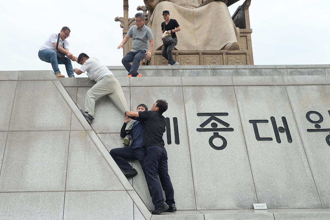 기아자동차 비정규직 노동자 4명이 27일 오전 10시경  '현대기아차그룹 정몽구 회장 구속' 등을 요구하는 기습시위를 벌이기 위해 서울 광화문광장내 세종대왕상으로 올라가자 주변에서 경계를 서던 경찰이 저지하고 있다.