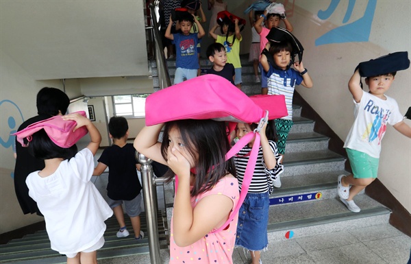 민방공 대피훈련을 한 23일, 대전 둔원초등학교 학생들이 공습 경보소리가 울리자 책가방을 머리 위로 올리고 신속하게 지하 강당으로 이동하고 있다.