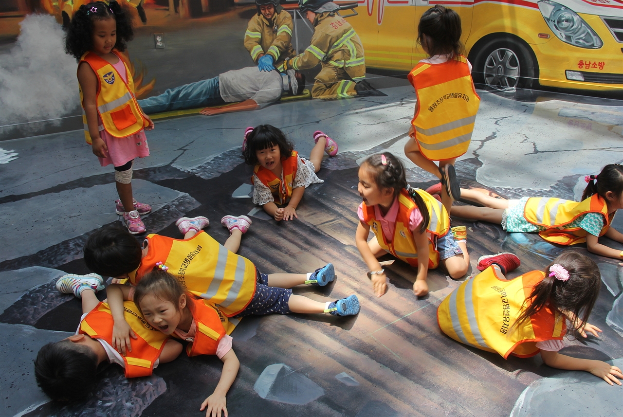 월랑초 병설유치원 만 4세반 아이들이 지진들이 갈라진 땅 그림위에 누워 구해달라고 요청을 하고 있다.   아이들이 즉석에서 만들어낸 안전 교육 놀이 퍼포먼스다.
