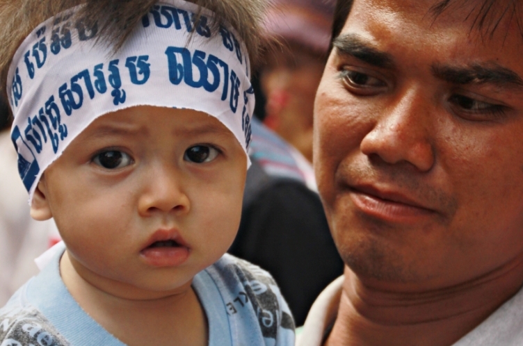 2013년 부정선거를 항의하기 위해 수도 프놈펜에서 열린 집회에 참가한 캄보디아 시민과 띠를 두른 어리 아기의 모습.