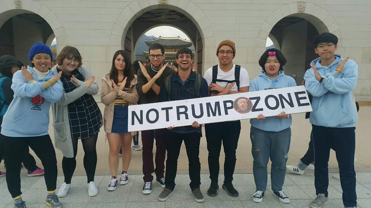 광화문 앞에서 '방미 트럼프 탄핵 청년 원정단' 단원들이 외국인 관광객들과 함께 노 트럼프 존 영상을 찍고 있다.