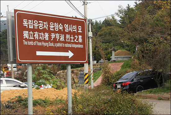 도로 가에 세워진 '독립유공자 윤형숙 열사의 묘' 안내판, 저 뒤로 열사의 무덤이 보인다.