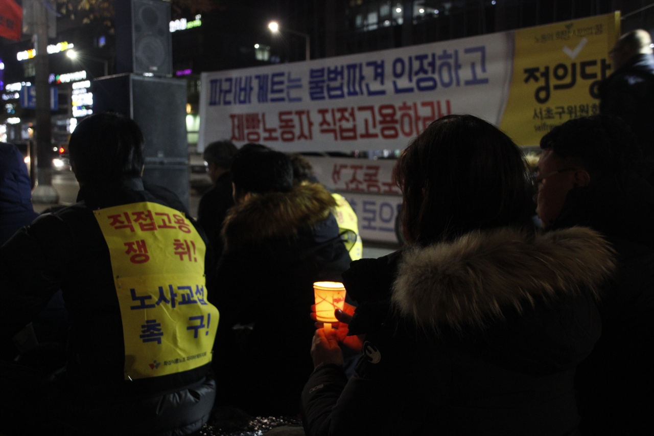  "직접고용 쟁취!" "노사교섭 촉구!" 몸자보를 바라보며 한 참가자가 촛불을 밝히고 있다