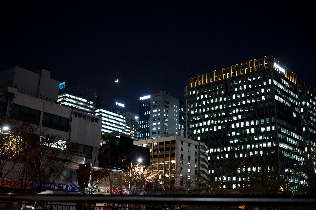 화려한 도시의 불빛 위로 달이 떠 있다.