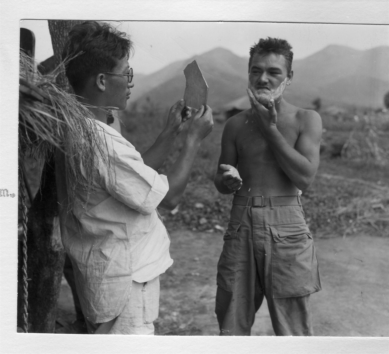 1950. 8. 25. 한 한국인이 거울을 들고 유엔군 병사의 면도를 도와주고 있다.