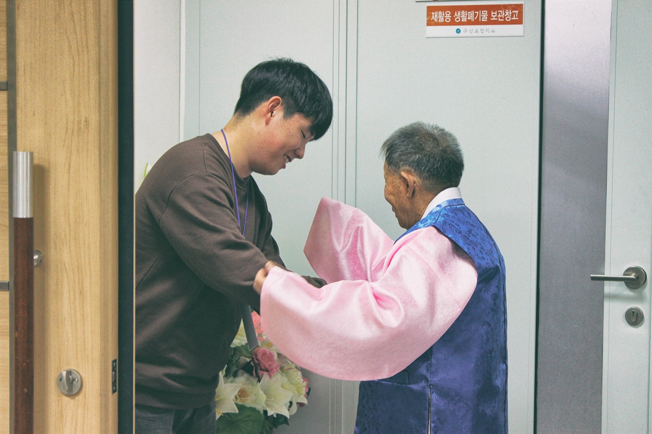 한복 착용을 도와드리는 청소년 봉사자의 모습. 어르신의 입가에 미소가 맺혀있다. (왼쪽 이민준 학생)