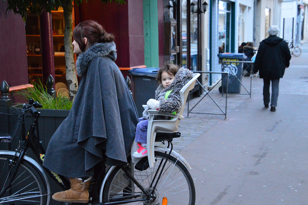 엄마 자전거 뒷좌석에 앉은 아이가 주변을 구경하고 있다.