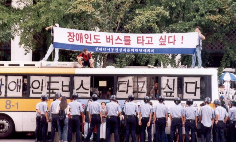  2000년대 초반 당시 장애인 이동권 투쟁. 적절한 직접행동 방식은 직접행동이 전달하고자 하는 메세지를 명확하게 전달하고, 목적 달성을 가로막는 <장애인 이동권 투쟁 보고서 ― 버스를 타자!> 중 한 장면. 지배적인 권력(혹은 기득권)이 무엇인지를 명확하게 드러내어 직접헹동을 더욱 효과적으로 만든다. 장애인 이동권 연대의 버스타기 투쟁은 장애인 이동권 투쟁이 무엇을 위한 투쟁인지를 아주 잘 보여주는 투쟁이었다고 생각한다.