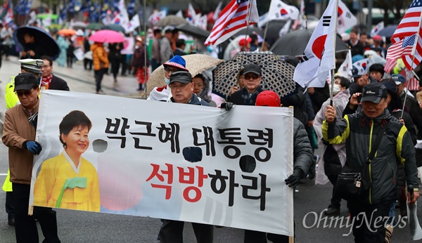 2018년 4월 14일 오후 서울 광화문광장 주변에서 박근혜 전 대통령 석방을 주장하는 주말집회가 열리는 가운데, 한 참가자가 태극기, 성조기, 이스라엘 국기를 들고 집회장으로 향하고 있다.