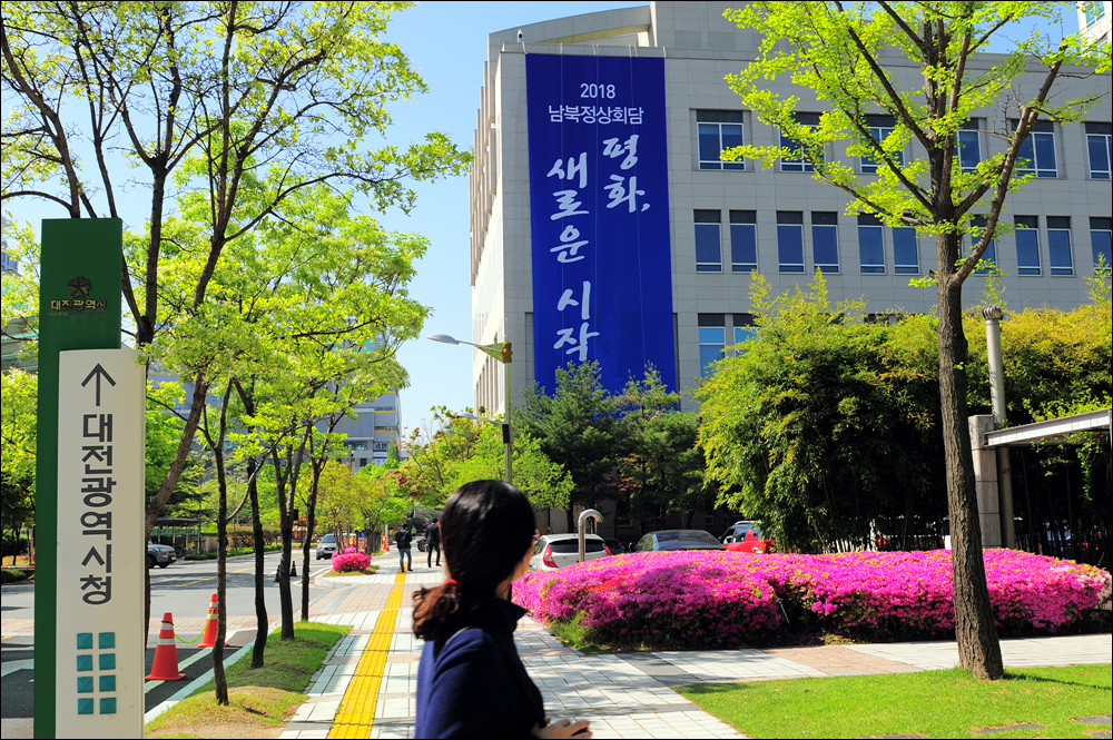  2018 남북정상회담의 표어 "평화, 새로운 시작'이라는 문구가 적힌 대형현수막이 대전광역시청사 외벽에 걸렸다. 지나가는 시민이 관심있게 현수막을 바라보고 있다.