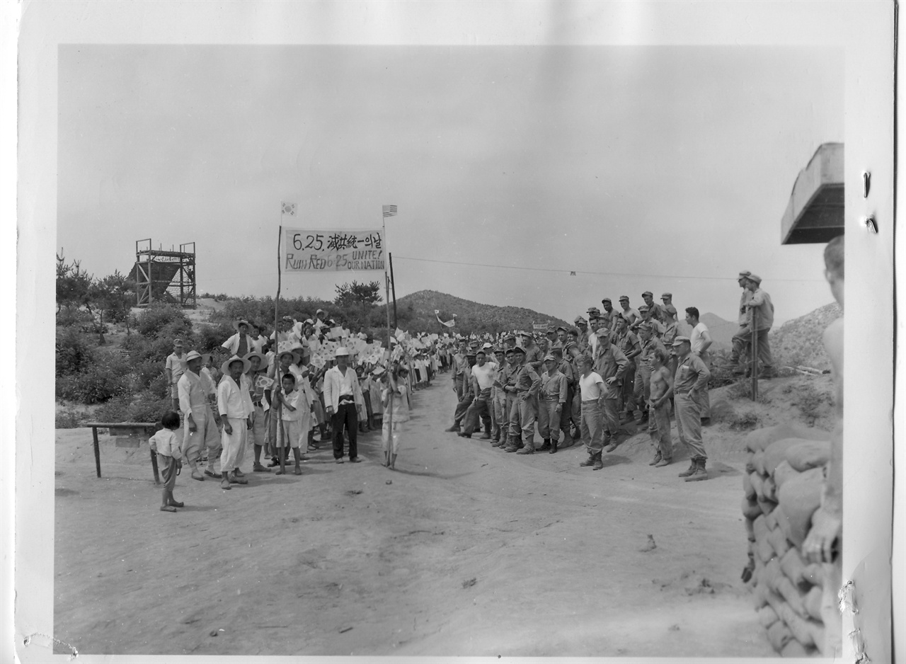  1952. 6. 25. 전방 부대 인근 마을 주민들이 6.25 전쟁 2주년 기념으로 ‘6.25. 멸공 통일의 날’ 플래카드를 장대에 멘 채 유엔군 부대 앞으로 행진을 하고 있다.