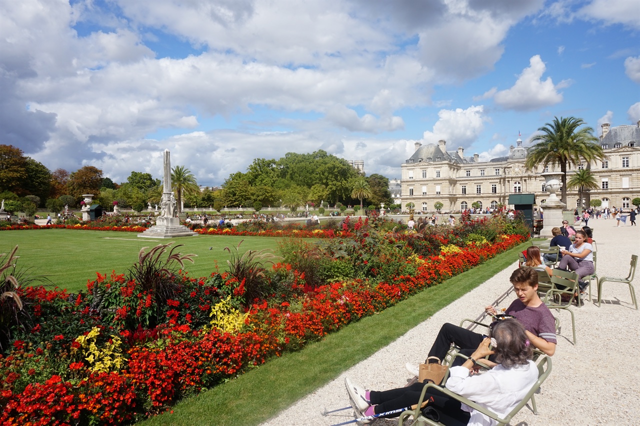 반쯤 드러누울 수 있게 만든 정원 앞 의자에 앉아 휴식을 취하고 있는 파리시민들. 오른쪽 뒤에 보이는 건물이 뤽상부르 궁전이다.