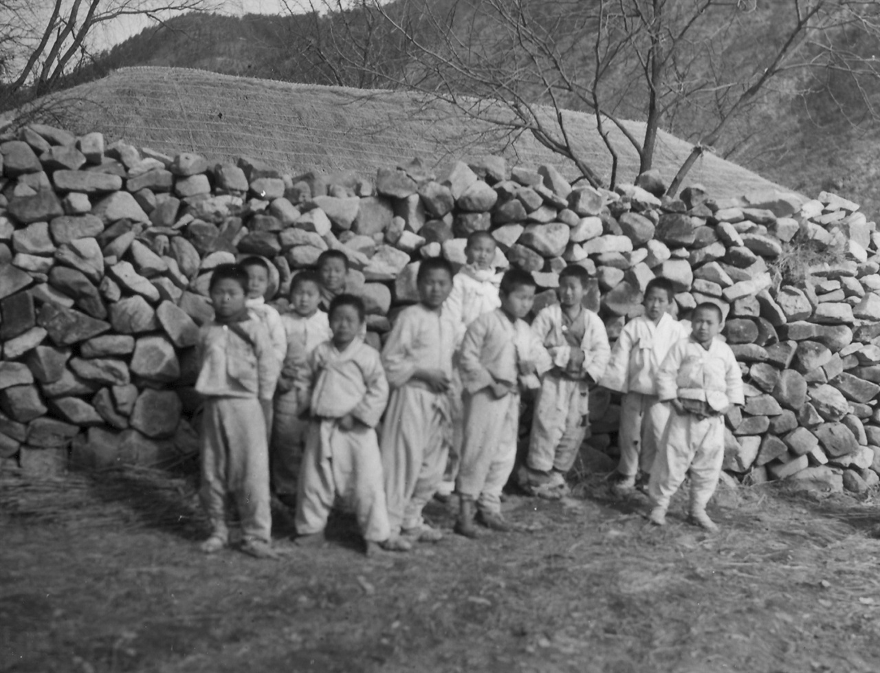 1951. 2. 6. 한국 산골마을 아이들이 돌담 앞에서 지나가는 유엔군들을 물끄러미 바라보고 있다.