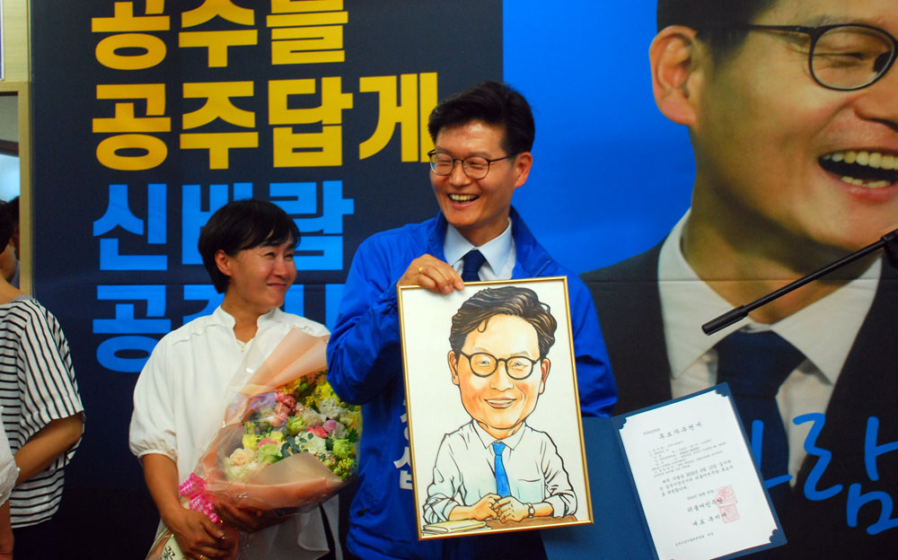 캐리커처와 꽃다발을 받은 김정섭 더불어민주당 후보와 부인이 환하게 웃고 있다.