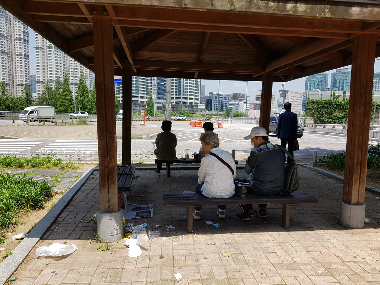 쉼터의 벤치에 앉은 두 시민이 주변에 널려 있는 쓰레기를 바라보고 있다.