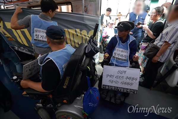  목에 요구사항이 적힌 피켓을 건 휠체어 장애인들이 지하철에 줄지어 탑승하고 있다.