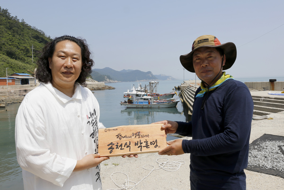  죽항도 포구에서 만난 진성영 작가와 송천식 씨. 서각 문패를 들고 자세를 한 번 취해달라는 부탁을 받고 마주 섰다.