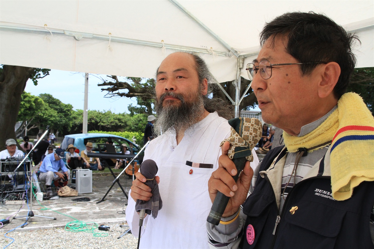 국제반전오키나와 집회에서 연설하고 있는 사진가 이시우 씨와 통역중인 평화 활동가 오오무라(大村)씨.