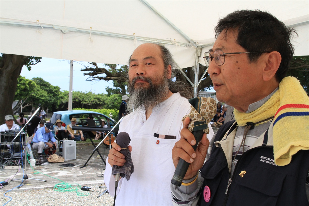  국제반전오키나와 집회에서 연설하고 있는 사진가 이시우 씨와 통역중인 평화 활동가 오오무라(大村)씨.