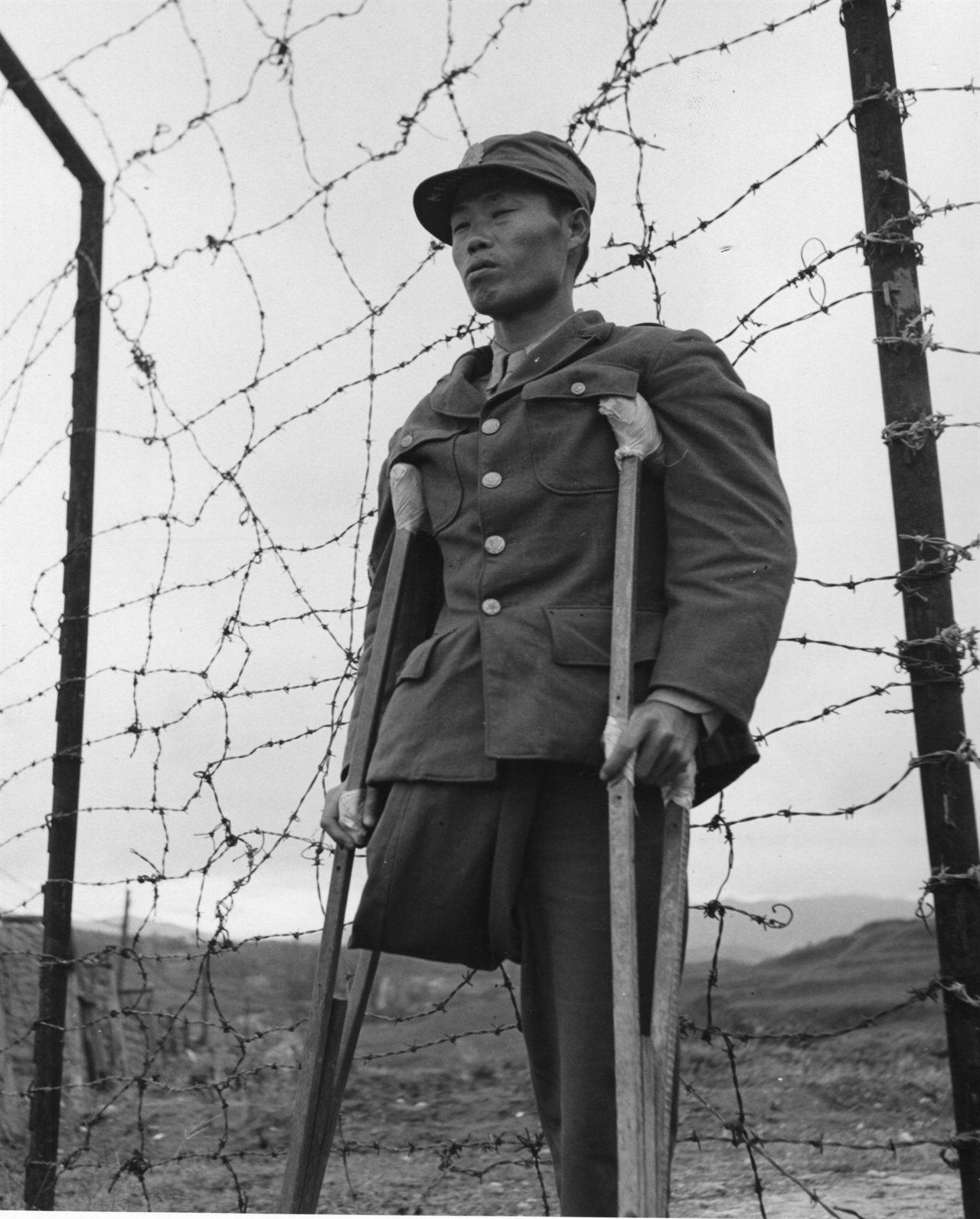 1950. 10. 옹진전투에서 한쪽 다리를 잃은 국군 특무상사가 목발을 짚은 채 침통한 표정으로 철조망 앞에 서 있다. 이는 전쟁에 신음하는 한반도를 상징하는 모습이 아닐까?