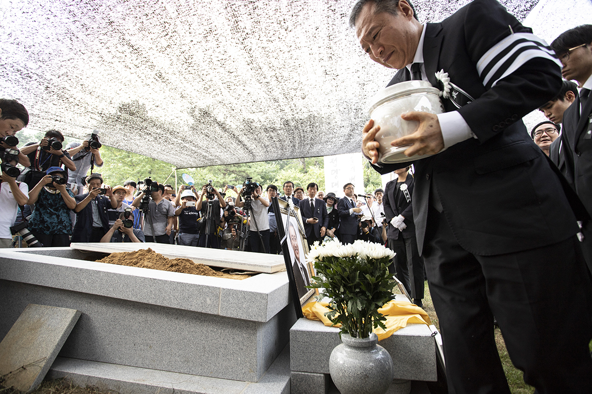 27일 오후 경기도 남양주시 모란공원에서 고 노회찬 정의당 원내대표의 하관식이 열린 가운데 고인의 친동생인 노회건씨가 고인의 유골을 묘소로 옮기고 있다. 