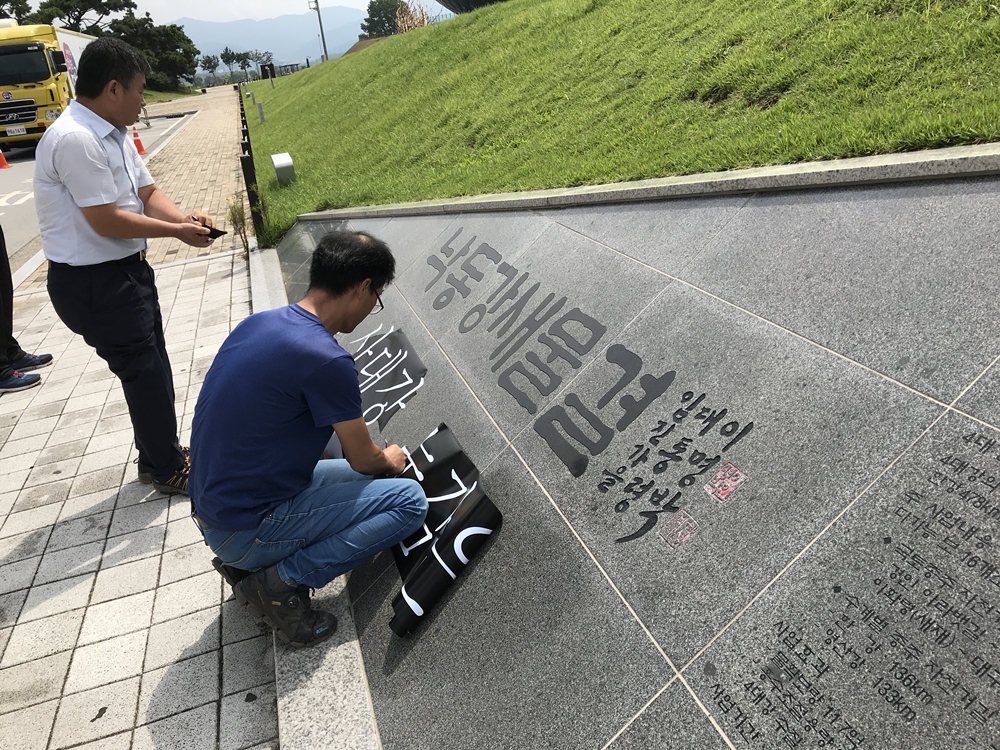 낙동강 새물결이라는 이명박 전 대통령의 휘호가 새개져 있는 기념석에 대구 작가들이 "죽어가는 4대강 눈감은 미술제 반대한다"는 문구가 박힌 시트지를 붙이고 있다 