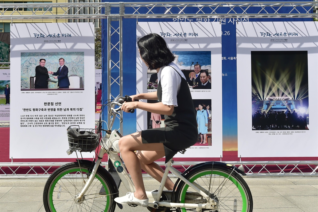 남북정상회담을 하루 앞둔 17일 오전 한반도의 평화를 기원하는 ‘평화, 새로운 미래’ 사진전이 서울 종로구 광화문광장에서 열리고 있는 가운데 한 시민이 자전거를 타고 가며 올해 개최된 남북정상회담시 촬영된 사진들을 바라보고 있다. 2018.09.17