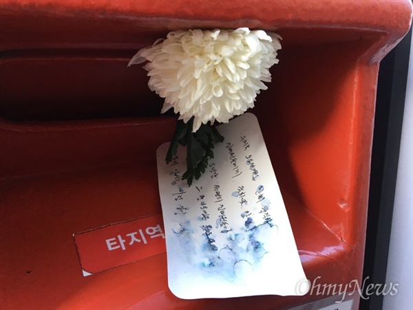 빨간 우체통에 꽂힌 하얀 국화꽃과 공개 편지