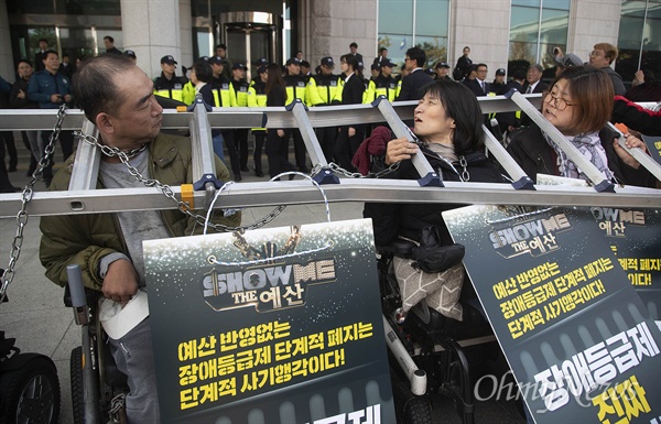 국회 기습 시위 벌이는 장애인들 "예산 반영 없는 장애등급제 단계적 폐지는 사기다” 전국장애인차별철폐연대 소속 장애인들이 5일 오후 서울 여의도 국회 의원회관 앞에서 자신의 몸에 사다리와 쇠사슬을 묶고 “예산 반영없는 장애등급제 단계적 폐지는 사기이다”며 장애인 복지를 위한 예산확대와 장애인 수용시설 폐지 등을 요구하며 기습시위를 벌이고 있다.