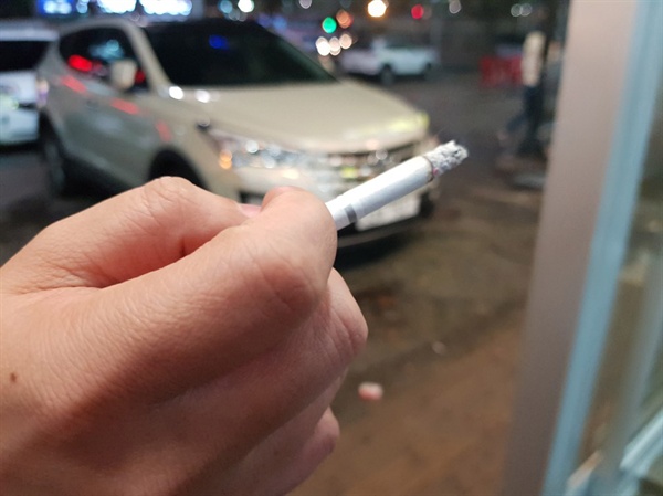 음식점 앞에서 흡연하고 있는 흡연자의 손에 있는 담배