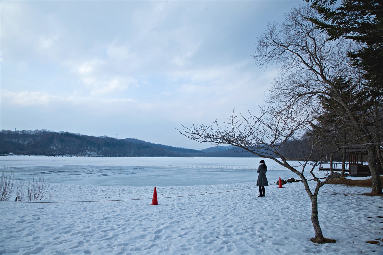 얼어붙은 홋카이도의 호수를 바라보는 여행자. 시적인 풍경이다.
