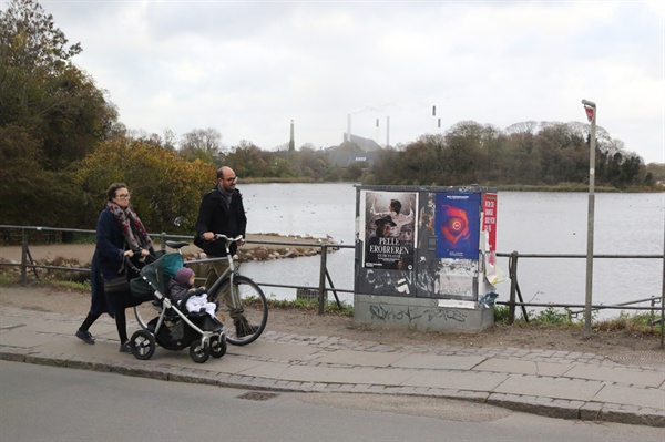 자전거와 아이를 태운 유모차를 끌고 여유로운 일상을 즐기고 있는 덴마크 국민들. 뒤로는 열병합 발전소가 보인다.
