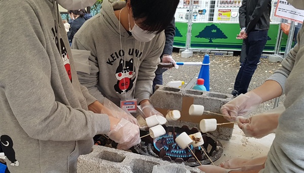 게이오대학 대학축제에서 먹거리천막에 참가한 학생들이 떡을 꼬치에 꿰어 굽고 있다.