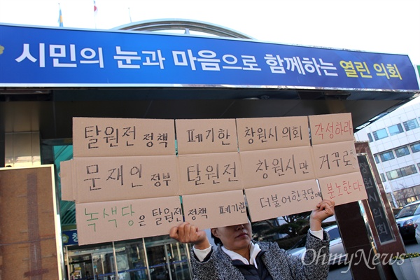 창원시의회가 '정부의 탈원전정책 폐기 촉구 결의문'을 채택한 가운데, 12월 13일 오전 한 시민이 창원시의회 앞에서 비난하는 손팻말을 들고 서 있다.