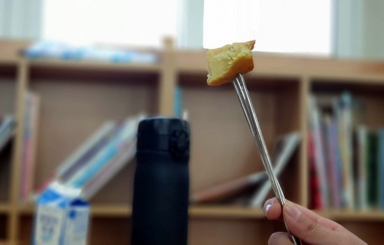 한 초등학생이 교실에서 학교 급식 시간에 젓가락으로 음식을 찍어먹고 있다. 