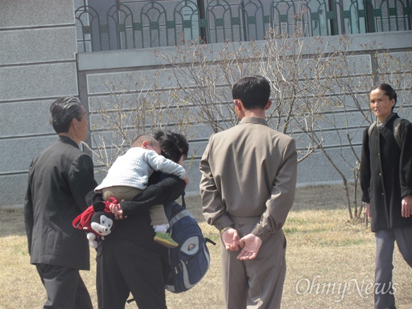 이고 지고 힘겹게 걸어가는 부인을 빤히 쳐다 보며 뒷짐 지고 걸어가는 북한의 한 남편(2012년 4월 18일 평양).