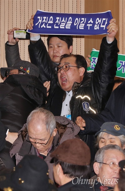 '5.18 북한군 개입설'을 주장하고 있는 지만원씨가 지난 8일 오후 서울 여의도 국회 의원회관에서 자유한국당 김진태·이종명 의원 공동주최로 열린 '5·18 진상규명 대국민 공청회'에 발표자로 나서자, 이에 반대하는 시민들이 '진실은 거짓을 이길 수 없다', '광주를 모욕하지 말라'라고 적은 플래카드를 펼치며 항의하고 있다.
