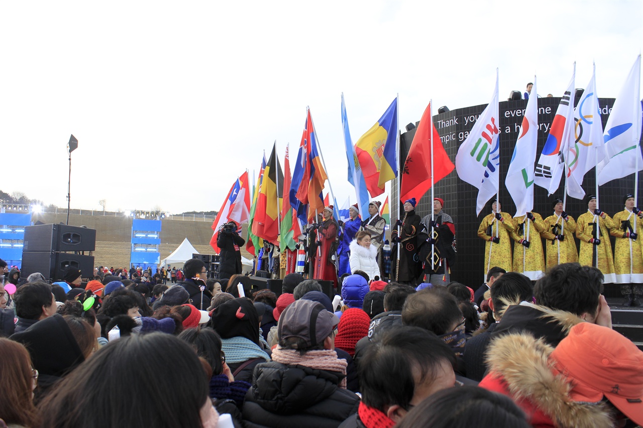 평창군기, 아지토스기, 태극기, 오륜기, 강원도기가 도열해 있다. 좌측으로는 올림픽 참가국 국기가 도열한 것이 보인다.