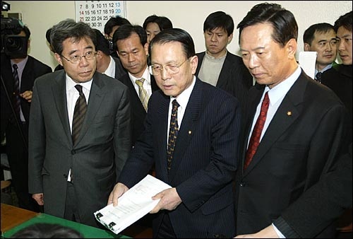 2004년 3월 12일 노무현 대통령 탄핵소추안이 국회를 통과한 뒤 김기춘 당시 국회 법사위원장(두 번째)이 탄핵 의결서 정본을 헌법재판소에 접수시키고 있다. 그 양 옆으로 한나라당과 민주당 법사위 간사인 김용균 의원과 함승희 의원이 보인다.