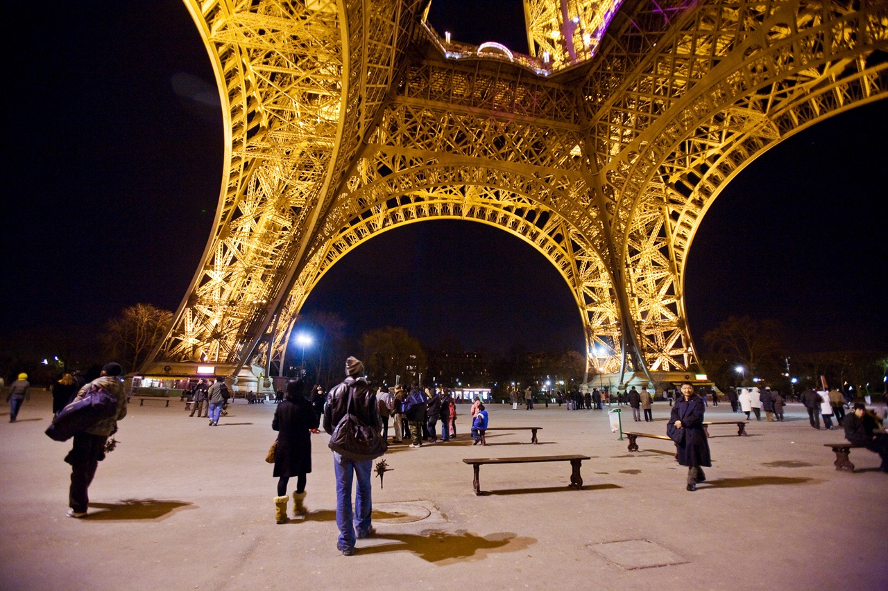 에펠탑 아래 석양의 파리 거리를 산책하는 관광객들.