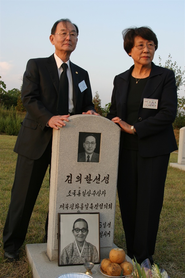 평양 용궁동 재북인사 묘역 아버지 묘비 앞에 선 김자동 회장 부부. 묘비 앞에 남에서 가져간 어머니 사진이 놓여있다.