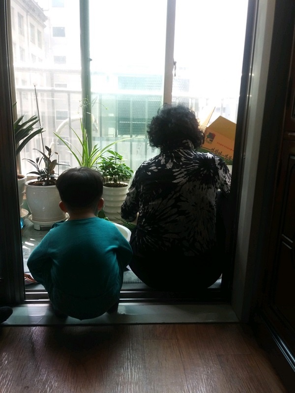 김치를 담그려고 채소를 다듬는 외할머니의 옆에 붙어앉아 함께하고 싶어하는 아이의 뒷모습.