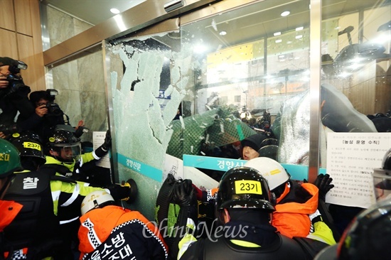 지난 2013년 12월 민주노총이 입주한 경향신문사 1층 현관 유리문을 열기위해 장비를 든 소방대원들이 투입되어 경찰이 노동자들이 막고 있던 유리문을 깨고 진입을 시도하고 있다.