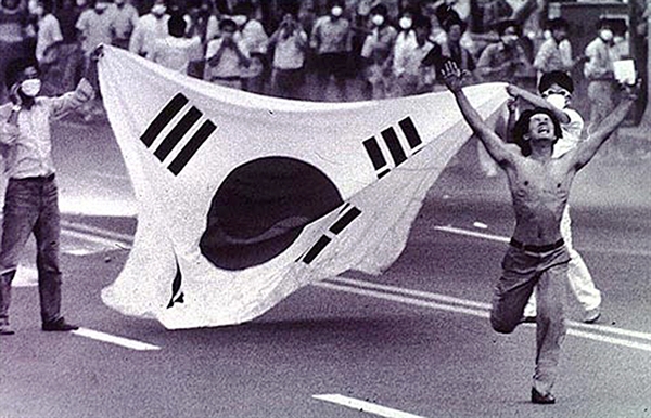 1987년 6월 항쟁을 상징하는 사진 한장. 한 청년이 태극기 앞으로 손을 들고 뛰쳐 나가고 있다.