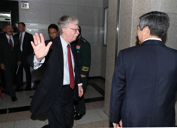 2019년 7월 24일, 존 볼턴 당시 미국 백악관 국가안보회의 보좌관이 서울 용산구 국방부를 방문, 정경두 국방부 장관의 안내를 받으며 이동중 취재진에 인사하고 있는 모습. 