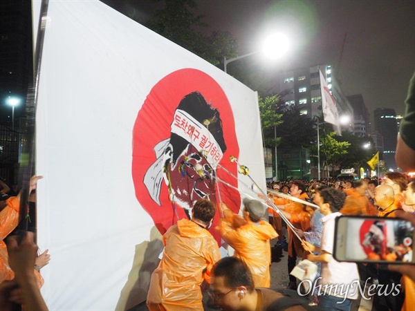 적폐청산사회대개혁 부산운동본부는 7월 27일 저녁 일본총영사관 앞에서 집회를 벌이며 아베 총리의 얼굴이 그려민 대형 펼침막에 페인트 세례를 가했다.