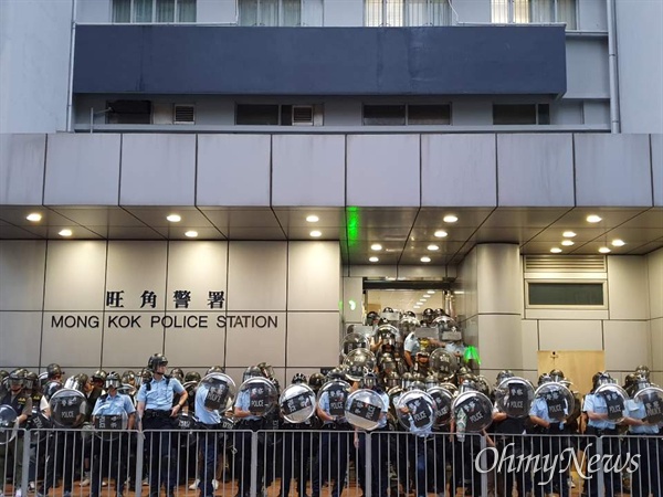 몽콕경찰서앞을 방패로 무장한 경찰들이 지키고 있다. 시민들이 경찰들을 향해 레이저포인트를 쏘고 있다.