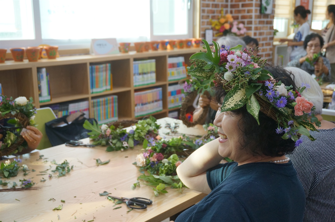 지난 24일 모가작은도서관에서 열린 '신나는 예술여행 우리동네 뒷동산 색깔전'에서 어르신이 꽃으로 화관을 만들어 쓰고 환하게 웃고 있다. 