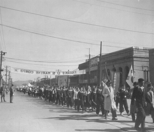 1950. 10. 27. 서울시민들이 “미 해병대 고맙습니다”라는 플래카드 아래에서 행진을 하고 있다.